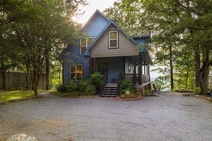 A blue house in the woods surrounded by trees.