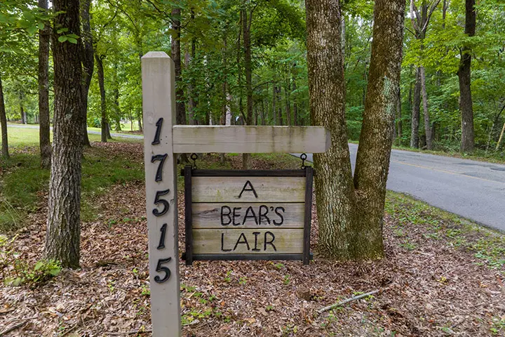 A sign for a bear's lair in a wooded area.