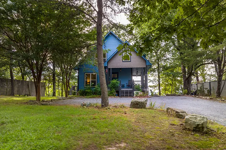 A blue house in the woods surrounded by trees.