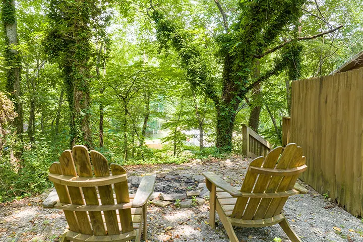 Two adirondack chairs in a wooded area.