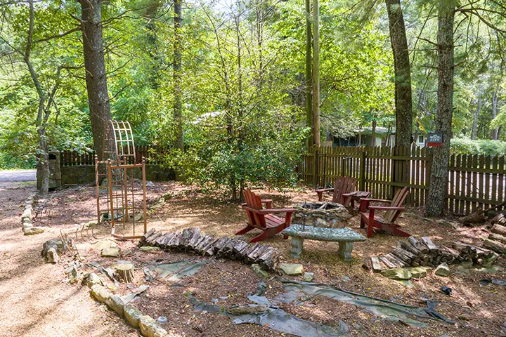 A wooded backyard with a fire pit and chairs.