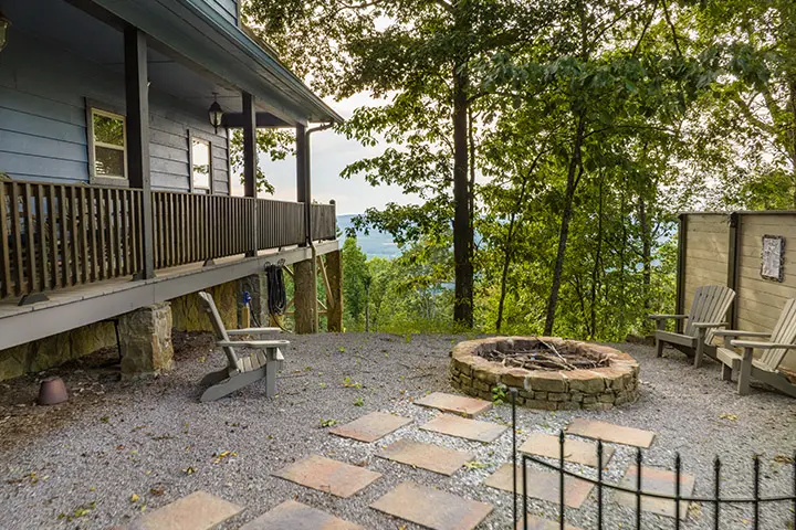 A patio with a fire pit overlooking a wooded area.