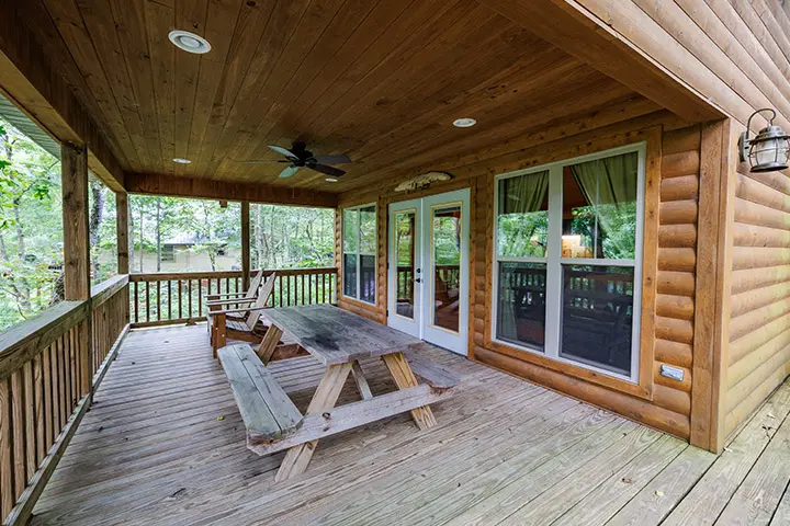 The porch of a log cabin with a table and chairs.