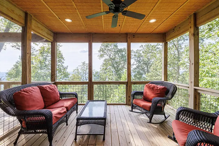 A screened in porch with wicker furniture and a ceiling fan.
