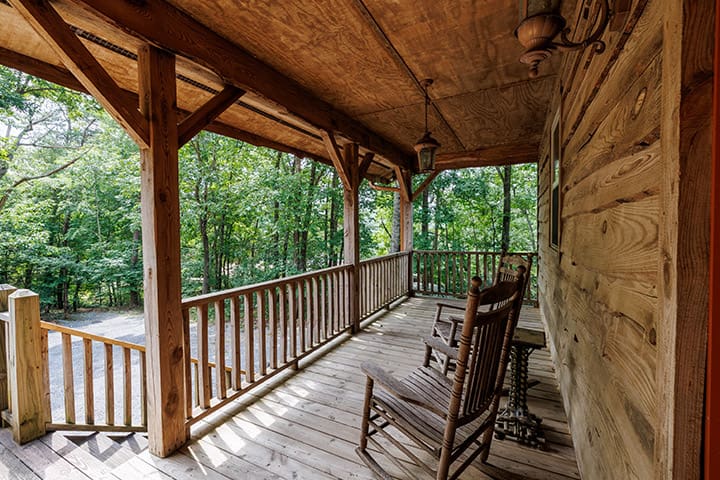 A wooden porch with rocking chairs and a view of the woods.