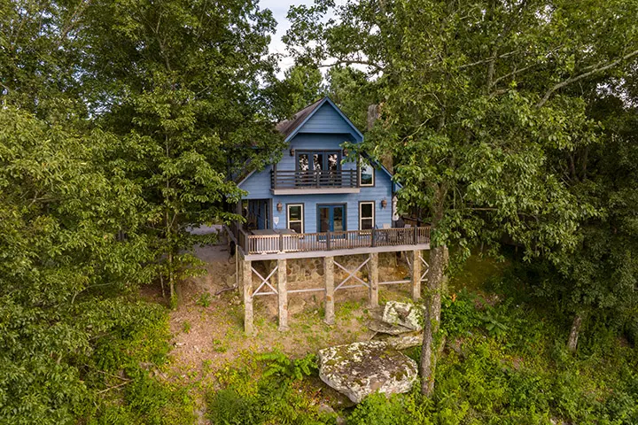 A blue house sits on top of a rock in the woods.