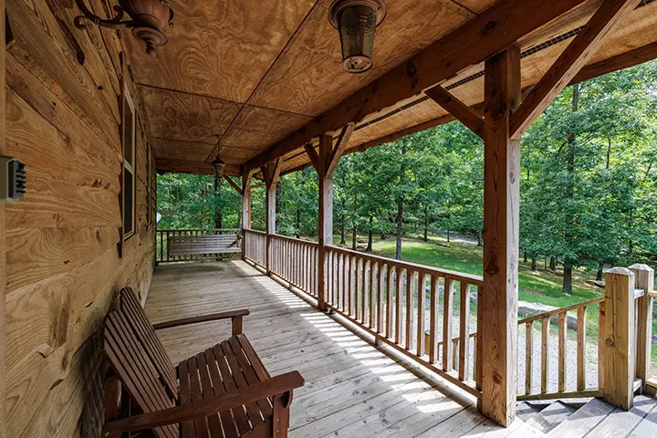 The porch of a log cabin with a wooden bench.