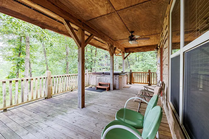 A deck with chairs and a hot tub in the woods.