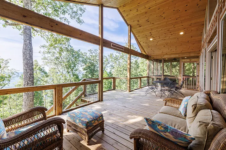 A deck with wicker furniture and a view of the woods.