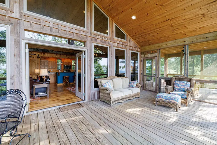 A screened in porch with wood flooring and furniture.