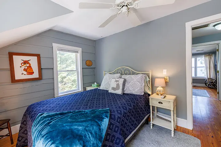 A bedroom with a ceiling fan and a blue comforter.