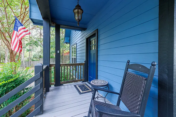 A blue porch with a rocking chair and an american flag.