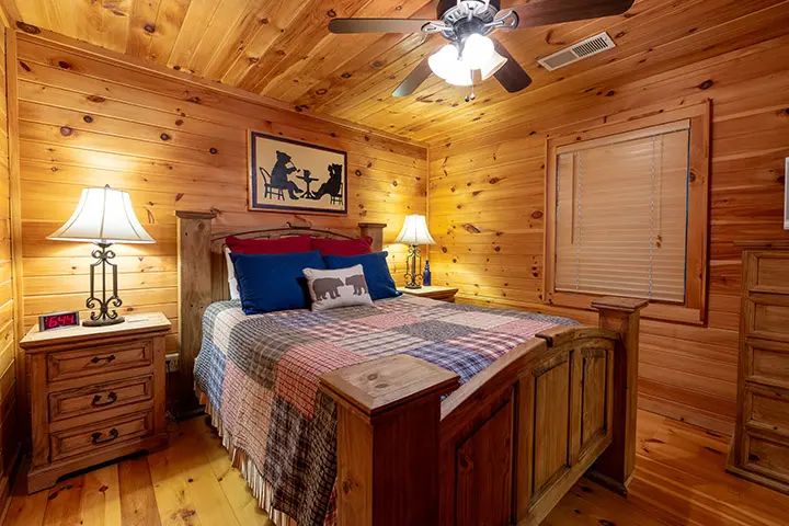 A bedroom in a log cabin with a bed, dresser, and ceiling fan.