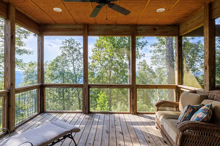 A screened in porch with wicker furniture overlooking a lake.