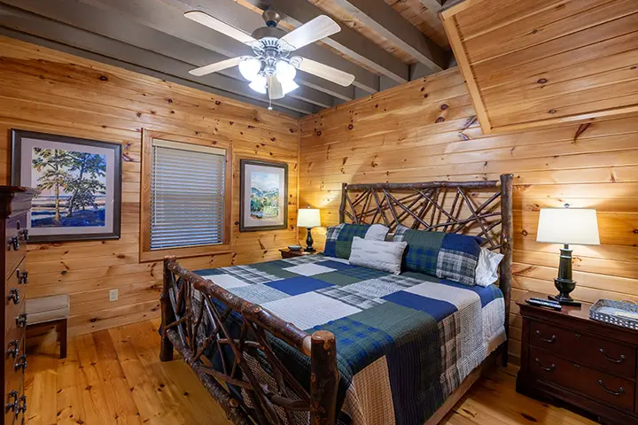 A bedroom in a log cabin with a bed and a ceiling fan.