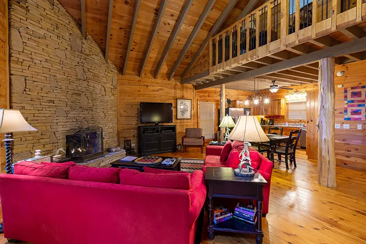 A living room in a log cabin with red couches and a fireplace.