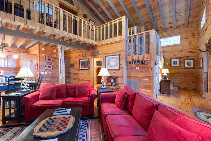 A living room in a log cabin with red couches and a tv.