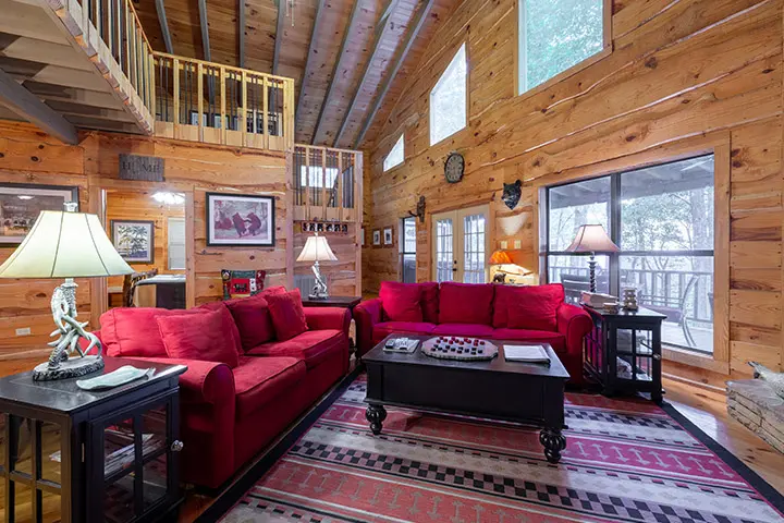 A living room in a log cabin with red couches and a fireplace.