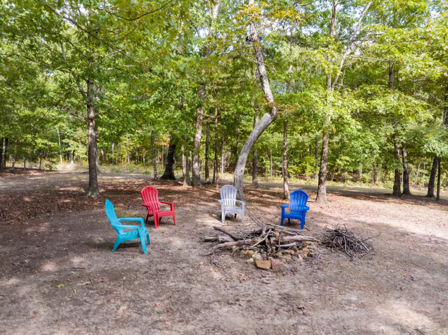 Four chairs sit around a fire pit in a wooded area.