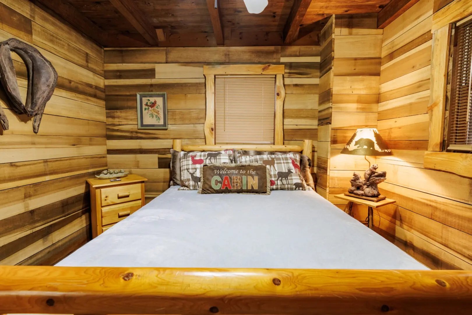 A cozy bedroom in a log cabin, perfect for a vacation getaway. The room features a comfortable bed and a fan to ensure optimal comfort during your stay.