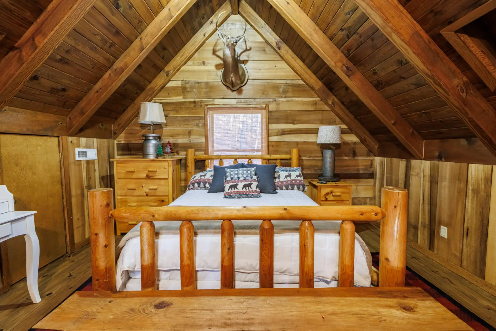 A cozy bedroom in a log cabin, perfect for a peaceful vacation getaway. The room features a comfortable bed and rustic decor, highlighted by a majestic deer head hanging proudly on the wall.