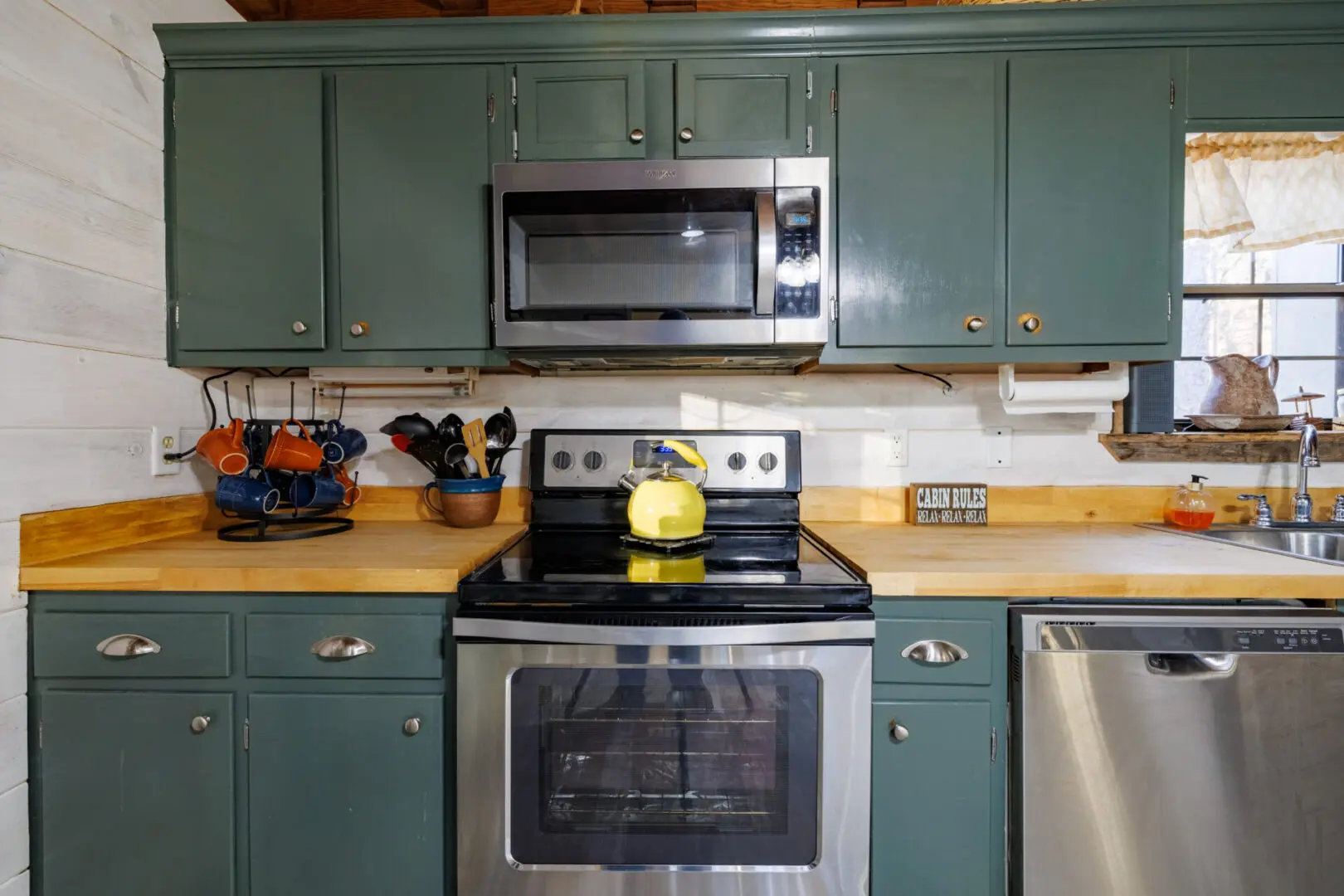 A vacation kitchen with green cabinets and a microwave.